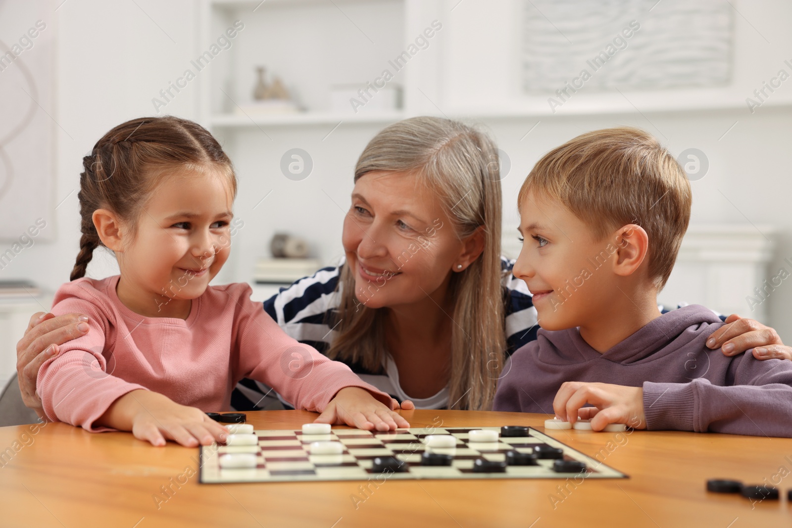 Photo of Family playing checkers at wooden table in room