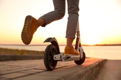 Photo of Woman riding electric kick scooter outdoors at sunset, closeup