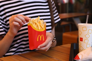 MYKOLAIV, UKRAINE - AUGUST 11, 2021: Woman with McDonald's French fries and drink at table in cafe, closeup