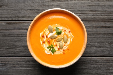 Photo of Bowl with tasty pumpkin soup on wooden table, top view