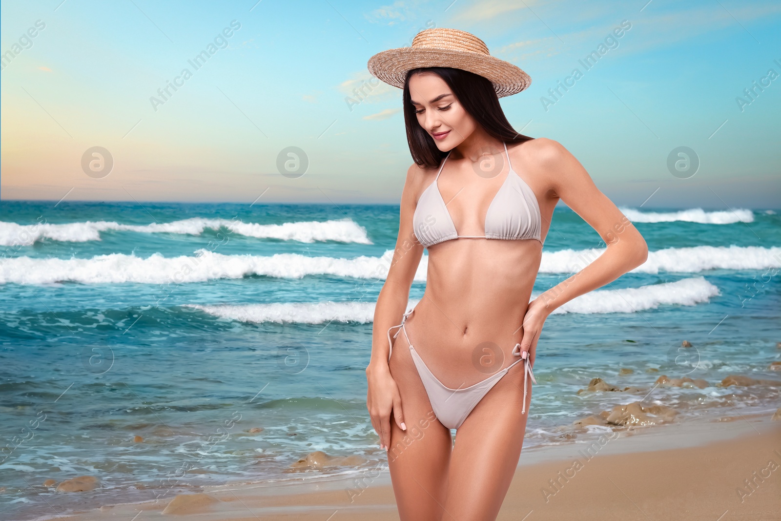 Image of Beautiful woman in stylish bikini and hat on sandy beach near sea, space for text