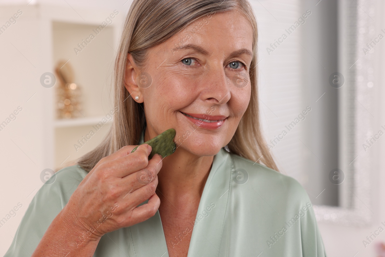 Photo of Woman massaging her face with jade gua sha tool in bathroom