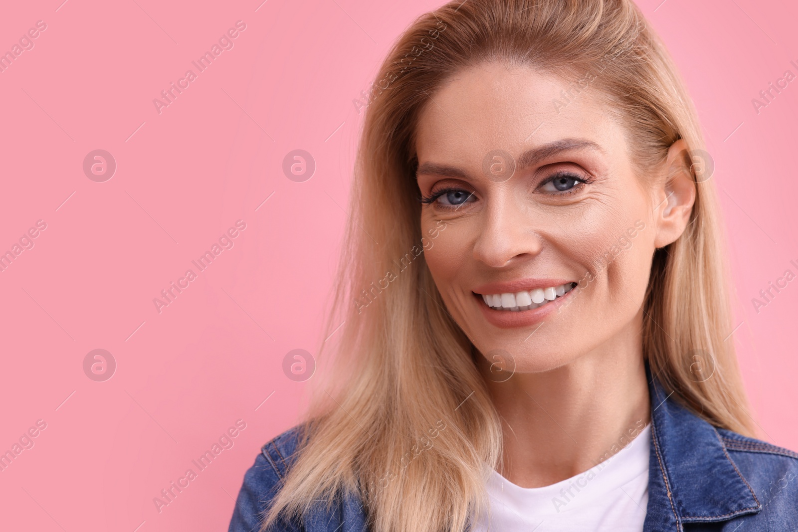 Photo of Portrait of smiling middle aged woman with blonde hair on pink background. Space for text