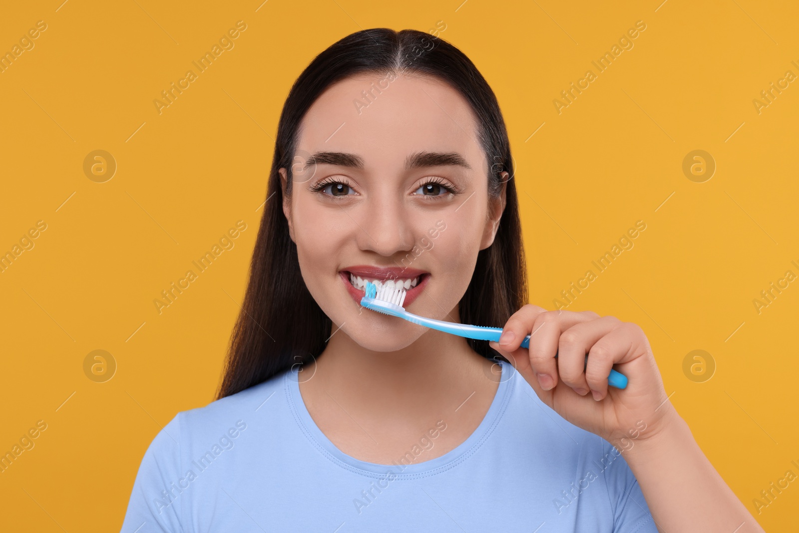 Photo of Happy young woman brushing her teeth with plastic toothbrush on yellow background