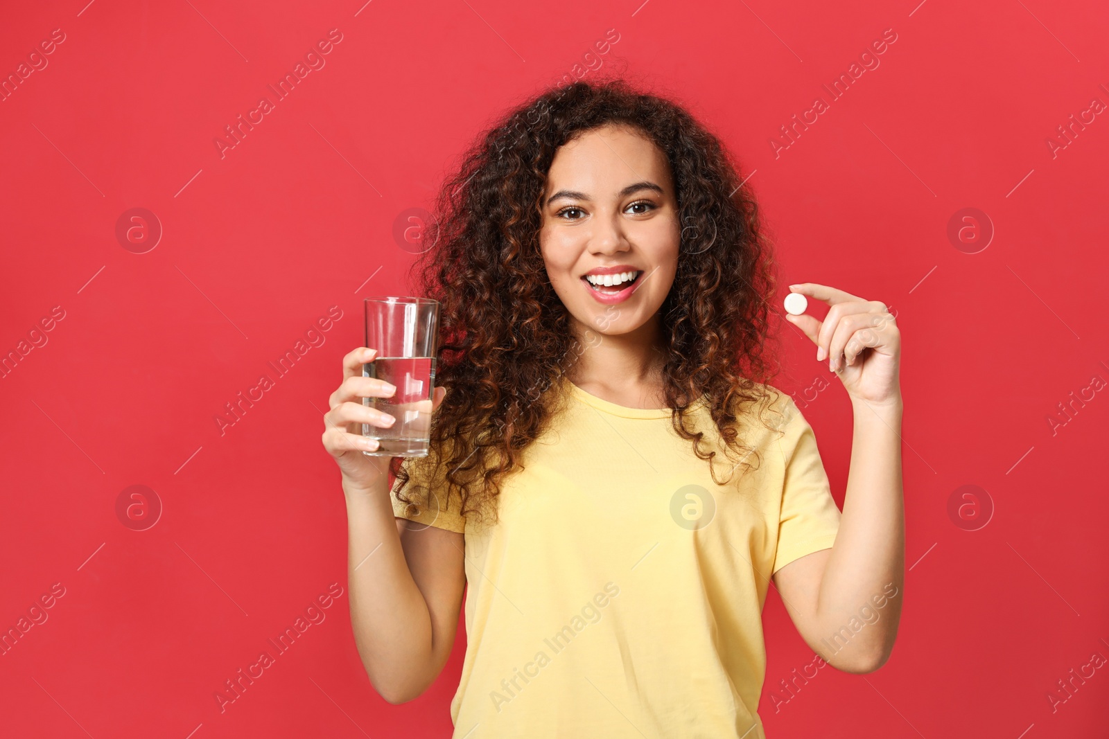 Photo of African-American woman with glass of water and vitamin pill on red background