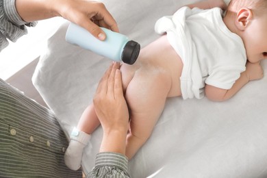 Photo of Mother applying dusting powder at baby's buttocks on changing table, above view