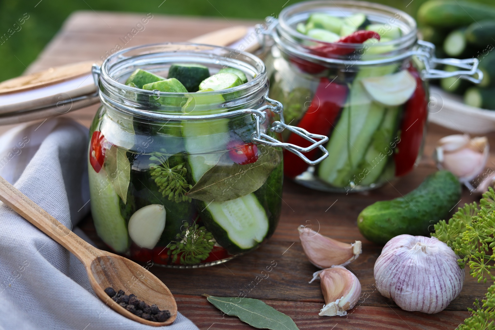 Photo of Glass jars with fresh cucumbers and other ingredients on wooden table, closeup. Canning vegetables