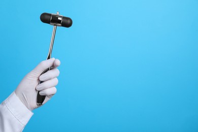 Photo of Doctor holding reflex hammer on light blue background, closeup with space for text. Nervous system diagnostic