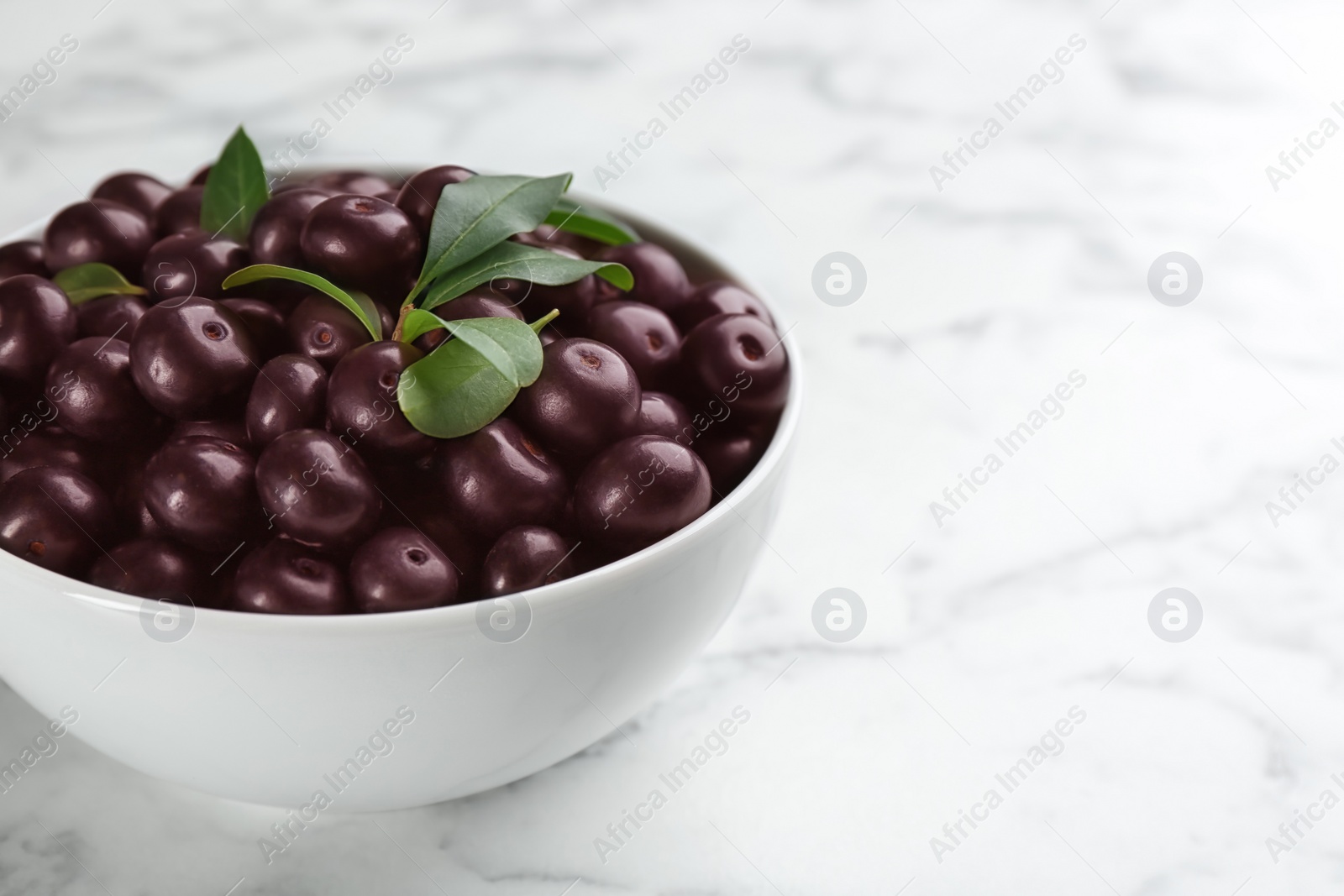 Photo of Fresh acai berries in bowl on white marble table, closeup. Space for text