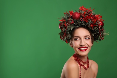 Beautiful young woman wearing Christmas wreath on green background. Space for text