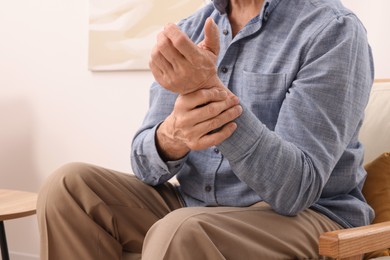 Senior man suffering from pain in his wrist at home, closeup. Arthritis symptoms
