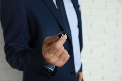 Photo of Stylish man holding cufflinks near white brick wall, closeup. Space for text