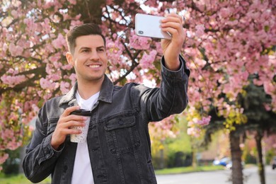 Photo of Happy man taking selfie with coffee outdoors on spring day