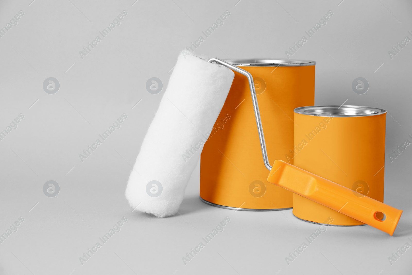 Photo of Cans of orange paint and roller brush on grey background. Space for text