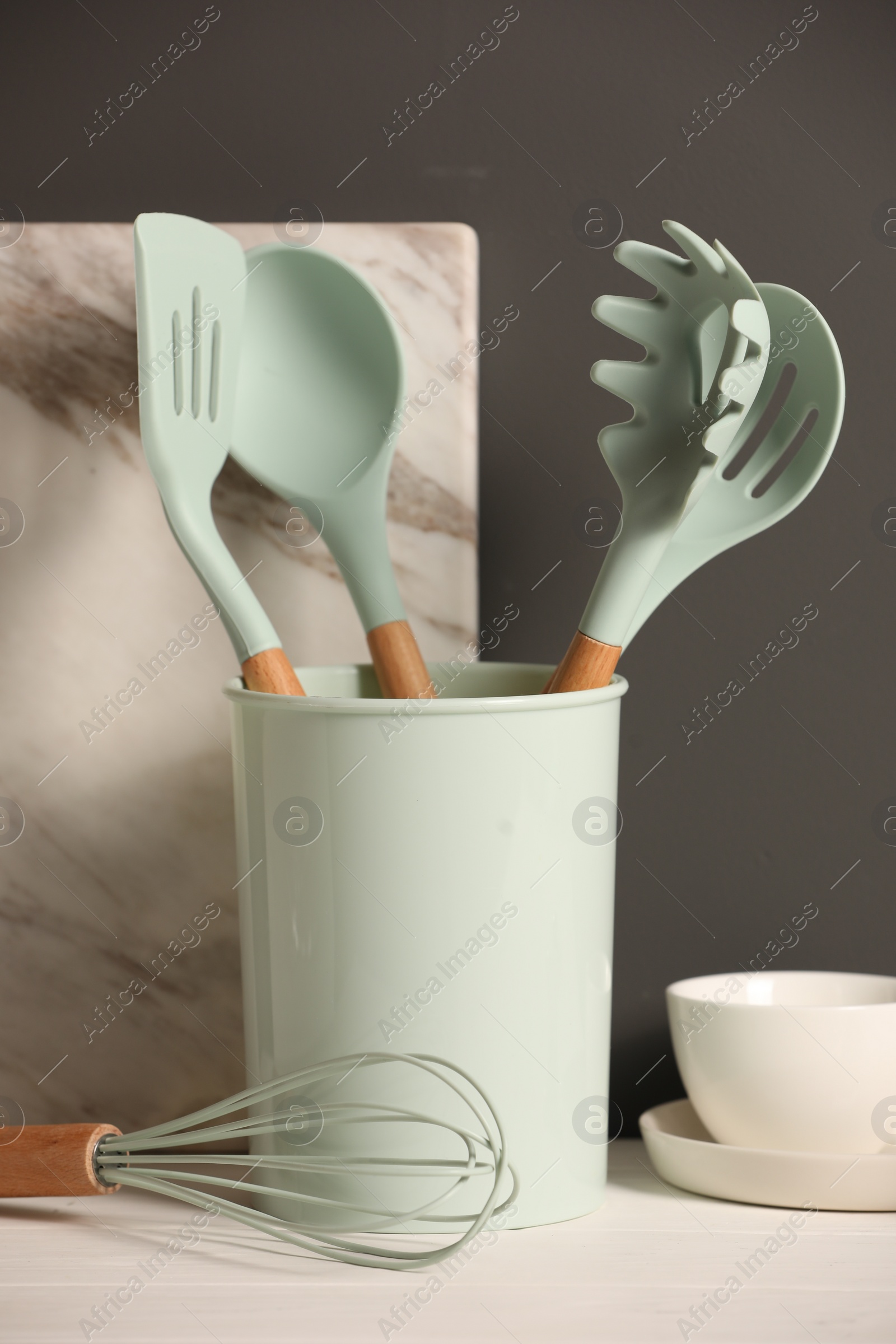 Photo of Set of different kitchen utensils on white wooden table against grey background