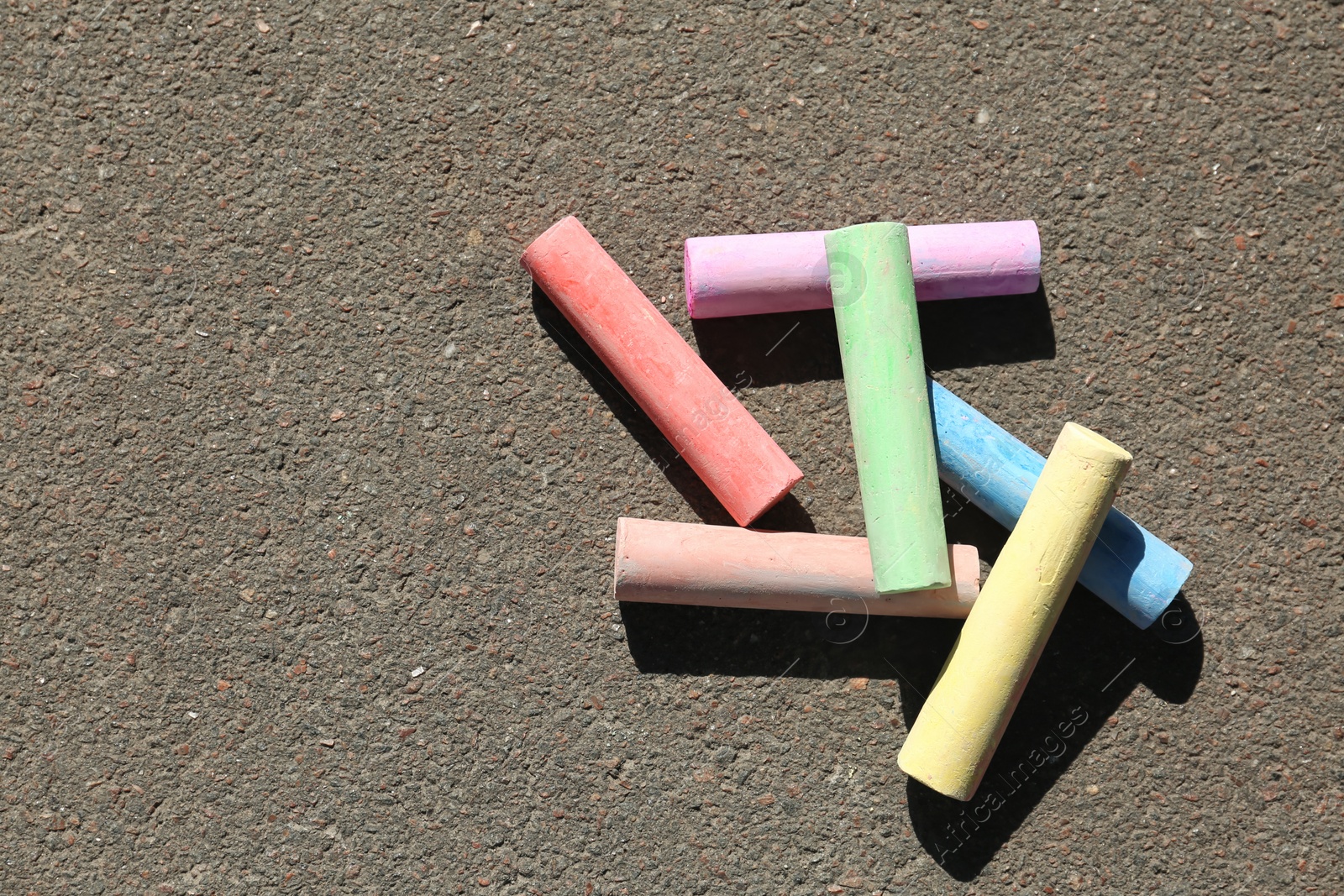 Photo of Colorful chalk sticks on asphalt, top view