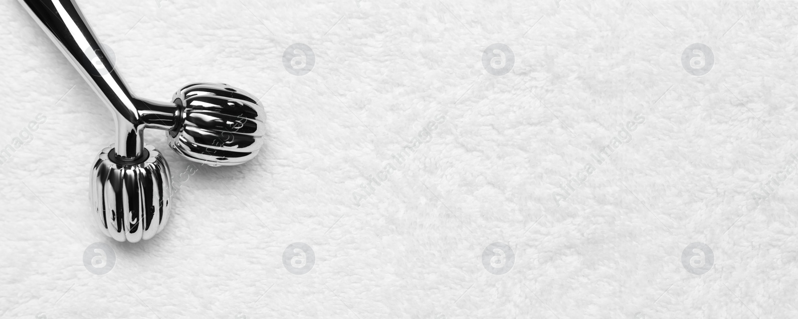 Image of Metal face roller on white towel, top view with space for text. Banner design
