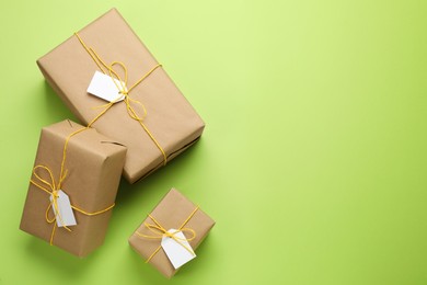 Photo of Parcels wrapped in kraft paper with tags on green background, flat lay. Space for text