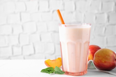 Tasty peach milk shake in glass and fresh fruit on white table. Space for text