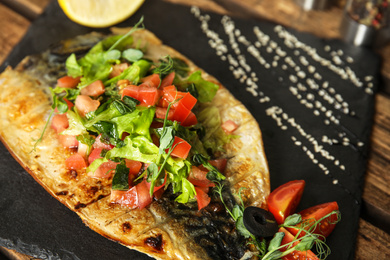 Photo of Delicious grilled fish with vegetables on slate plate, closeup