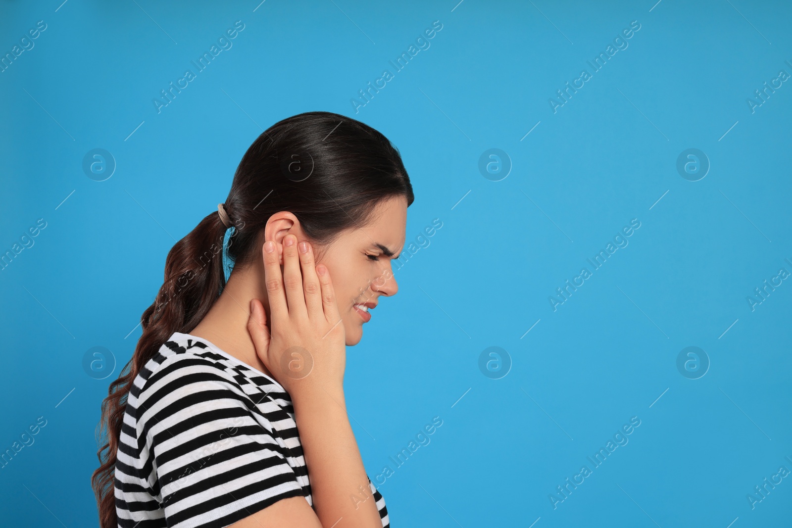 Photo of Young woman suffering from ear pain on light blue background, space for text