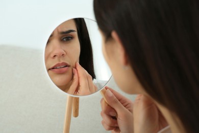 Photo of Young woman looking in mirror on her pimples indoors. Hormonal disorders