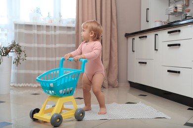 Cute baby with toy walker in kitchen near window. Learning to walk