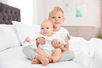 Photo of Cute boy sitting with his little sister on bed at home