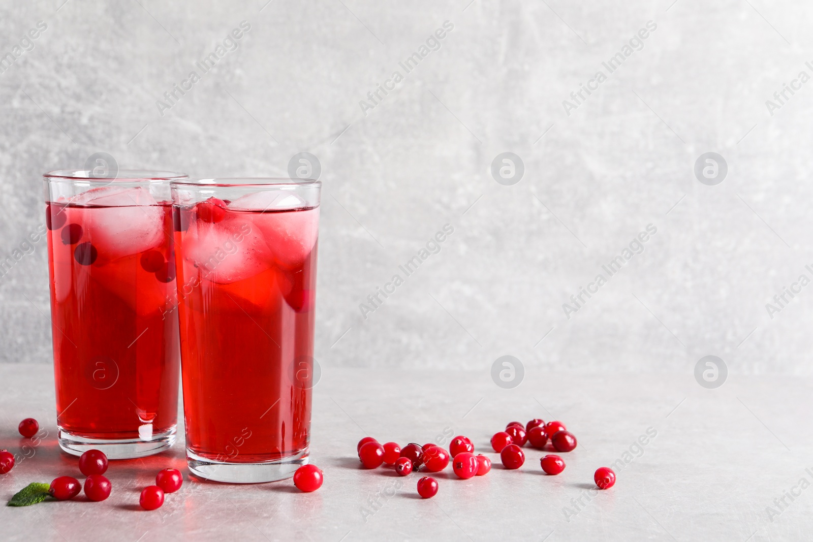 Photo of Tasty cranberry juice with ice cubes in glasses and fresh berries on light grey table, space for text