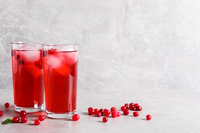 Tasty cranberry juice with ice cubes in glasses and fresh berries on light grey table, space for text