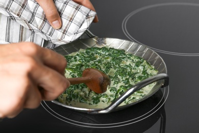 Photo of Woman cooking tasty spinach dip on kitchen stove, closeup view