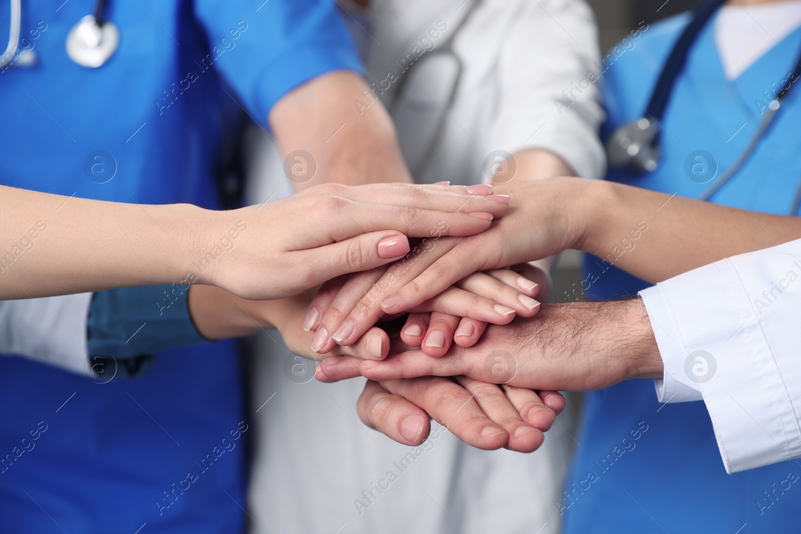 Photo of Team of medical doctors putting hands together indoors, closeup