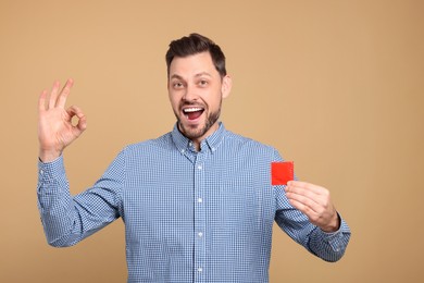 Photo of Excited man with condom showing ok gesture on beige background