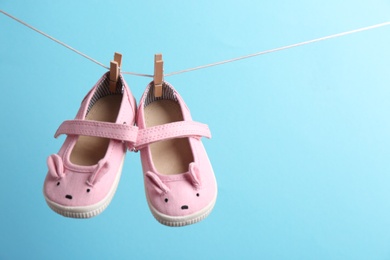 Photo of Cute small shoes hanging on washing line against color background, space for text. Baby accessories