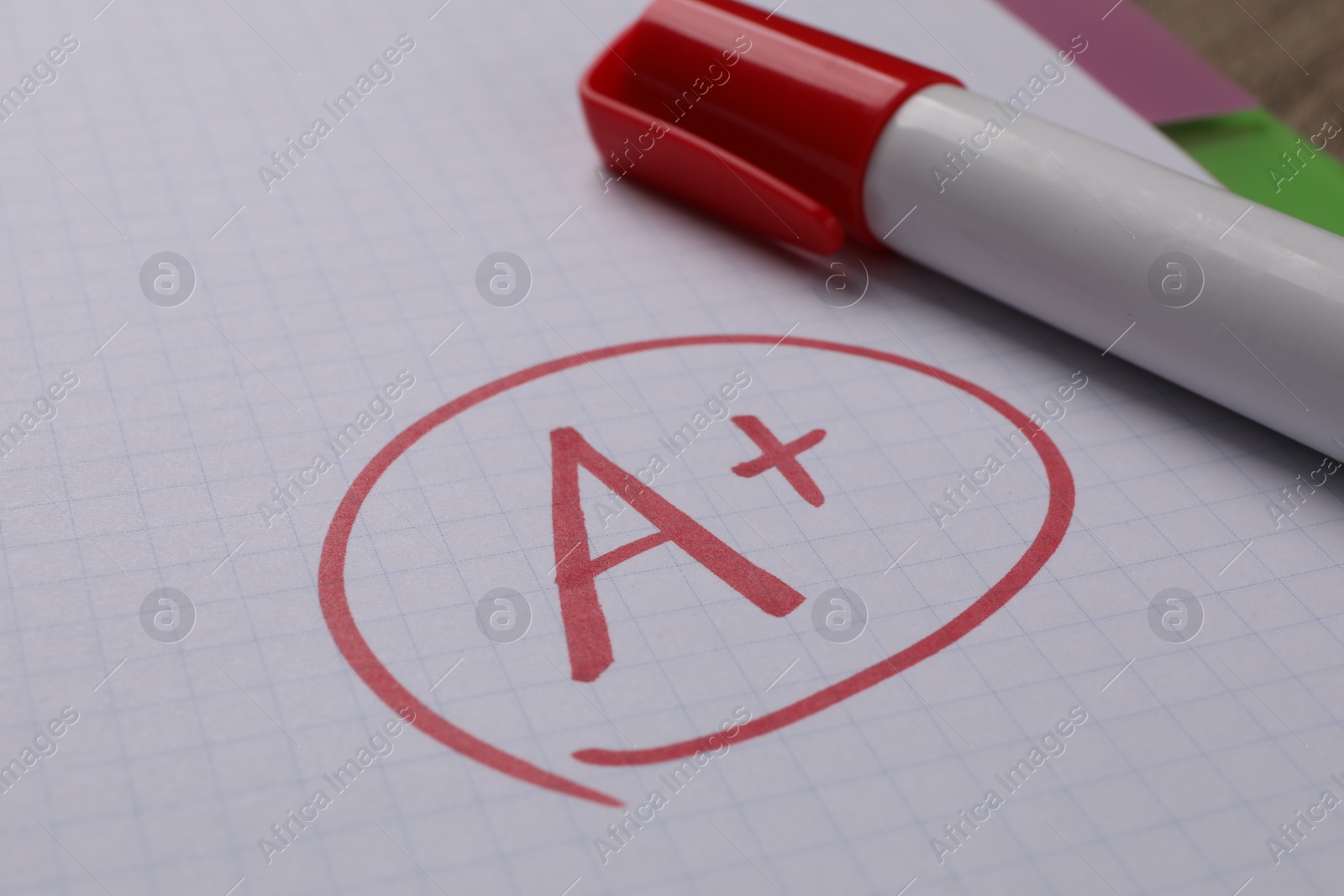 Photo of School grade. Red letter A with plus symbol on notebook paper and marker, closeup