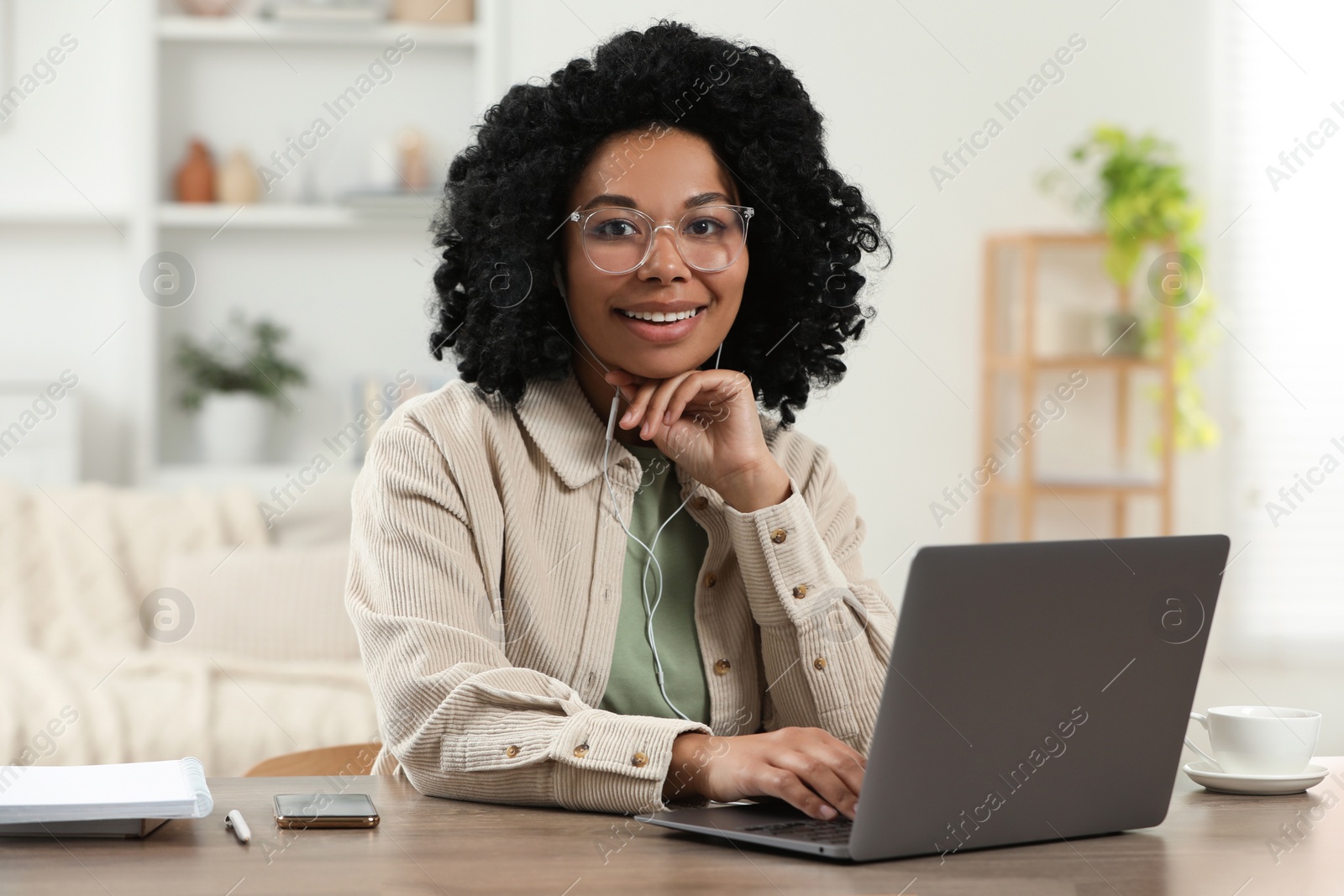 Photo of Happy young woman with laptop at wooden desk indoors