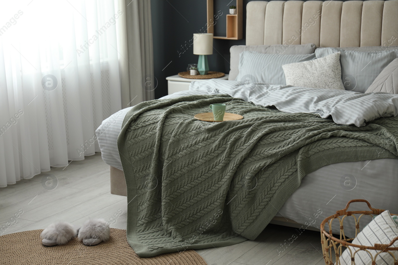 Photo of Comfortable bed with knitted green plaid in stylish room interior