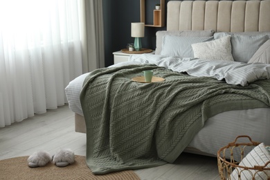 Photo of Comfortable bed with knitted green plaid in stylish room interior