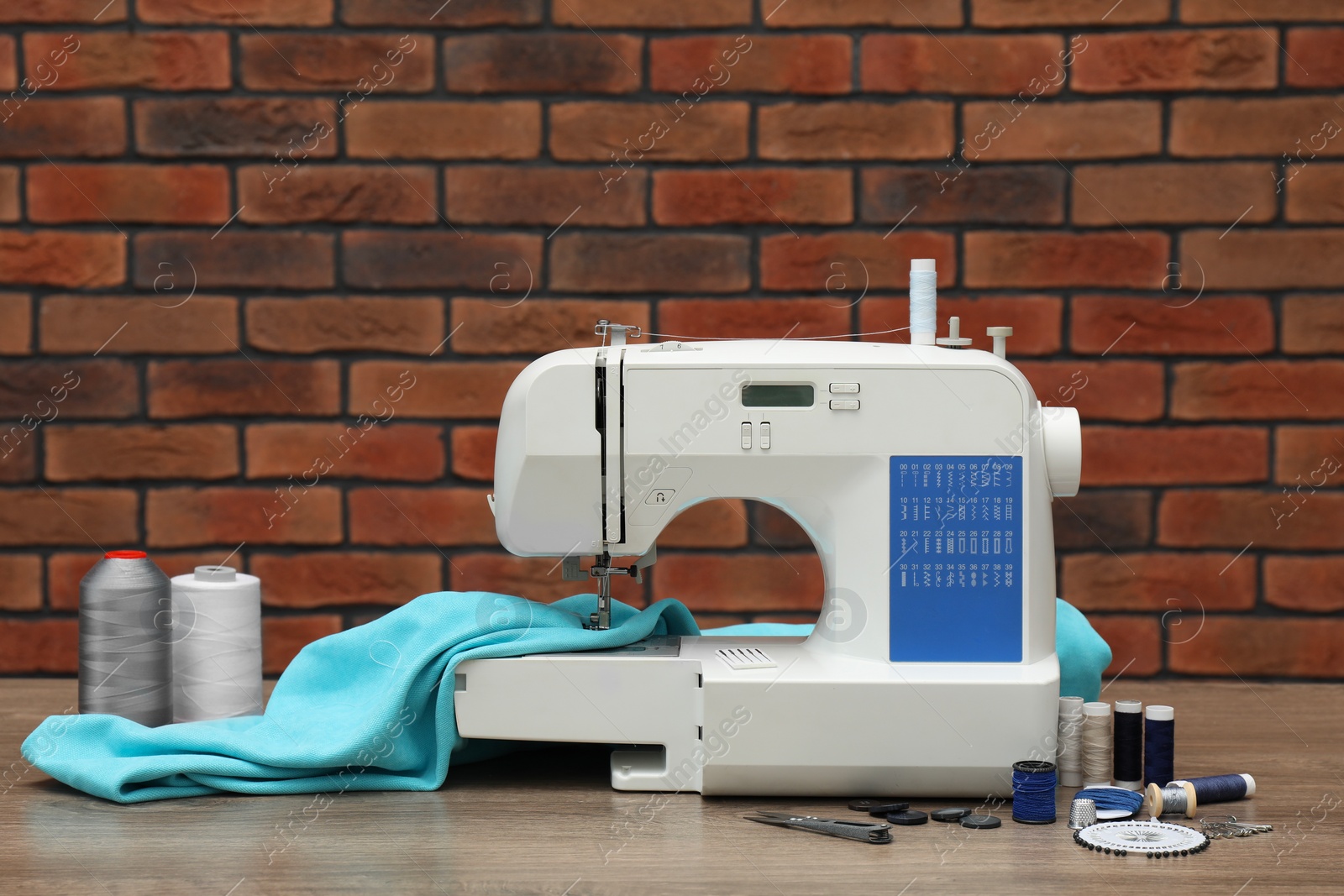 Photo of Sewing machine with fabric and craft accessories on wooden table against brick wall