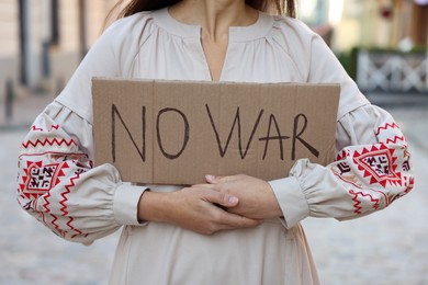 Photo of Woman in embroidered dress holding poster No War outdoors, closeup
