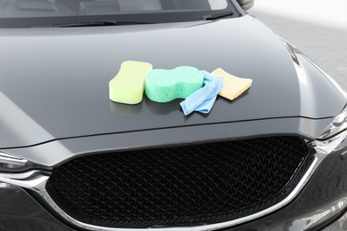 Photo of Sponges and rags on car hood outdoors. Cleaning products