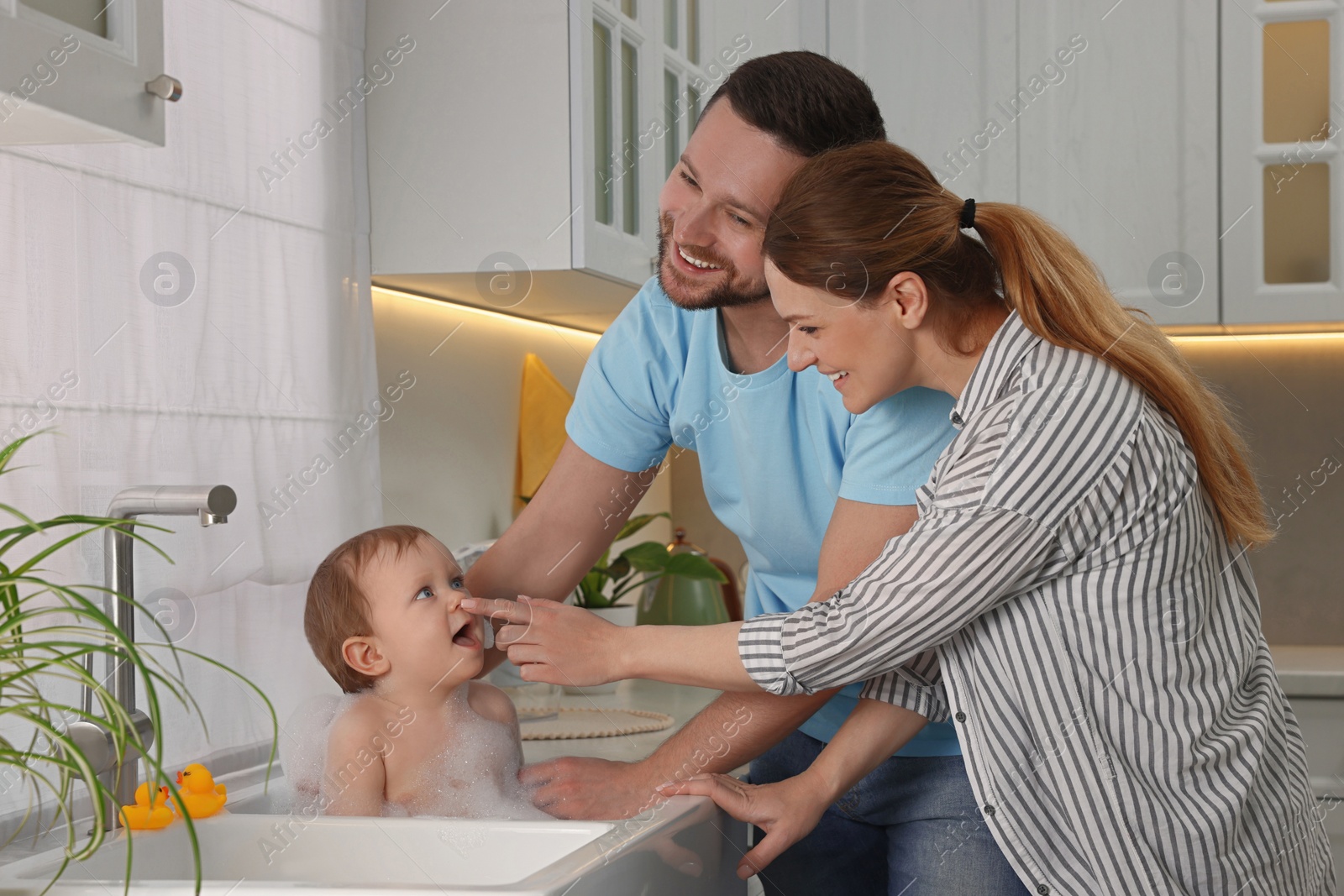 Photo of Father and mother washing their little baby in sink at home