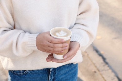 Photo of Woman holding takeaway cardboard cup on city street, closeup. Coffee to go