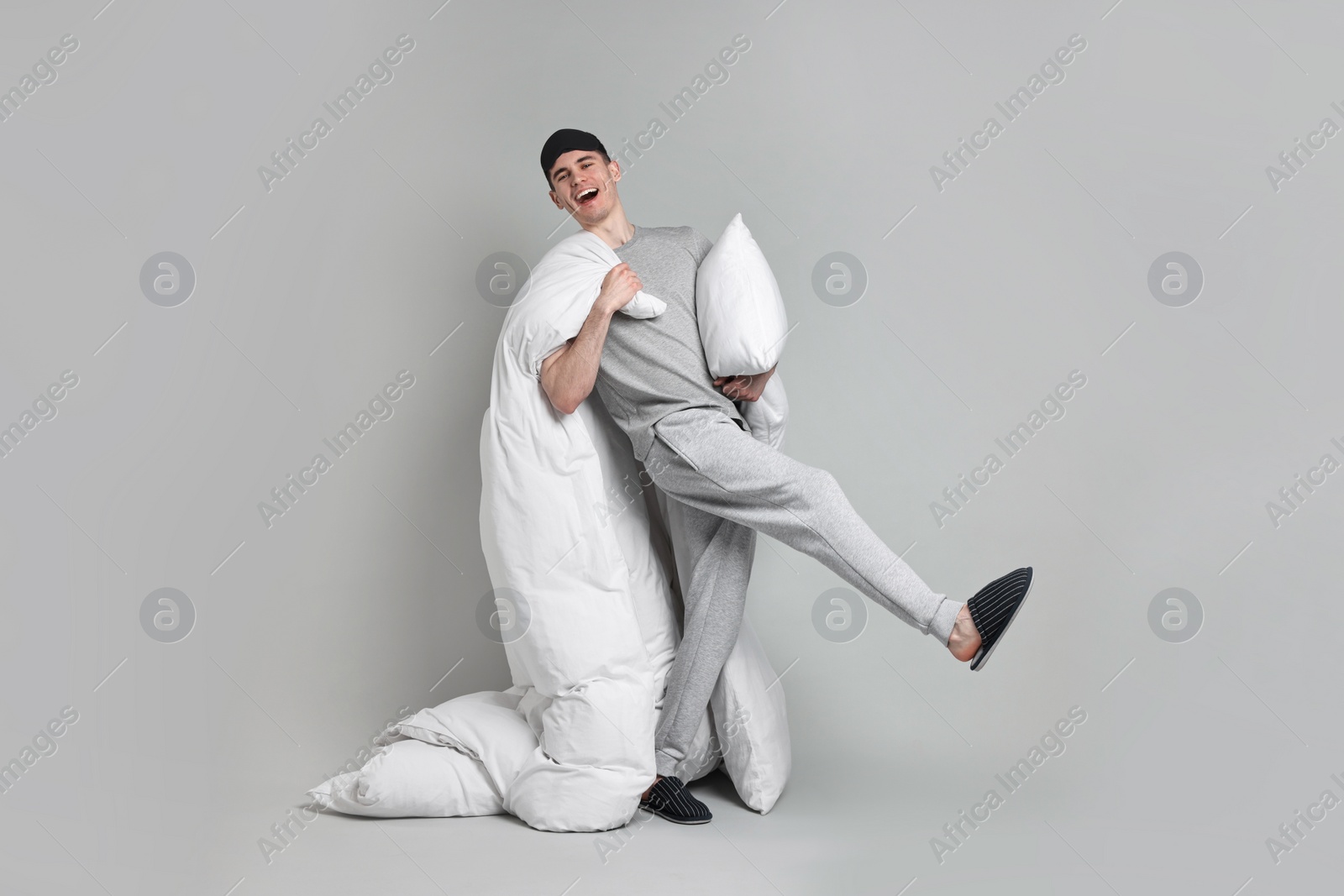 Photo of Happy man in pyjama holding pillow and blanket on grey background