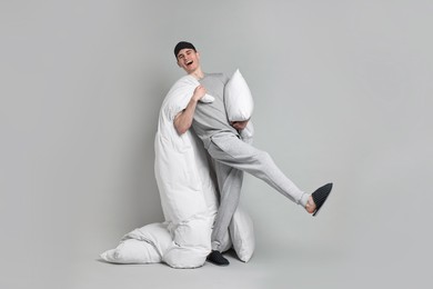 Photo of Happy man in pyjama holding pillow and blanket on grey background