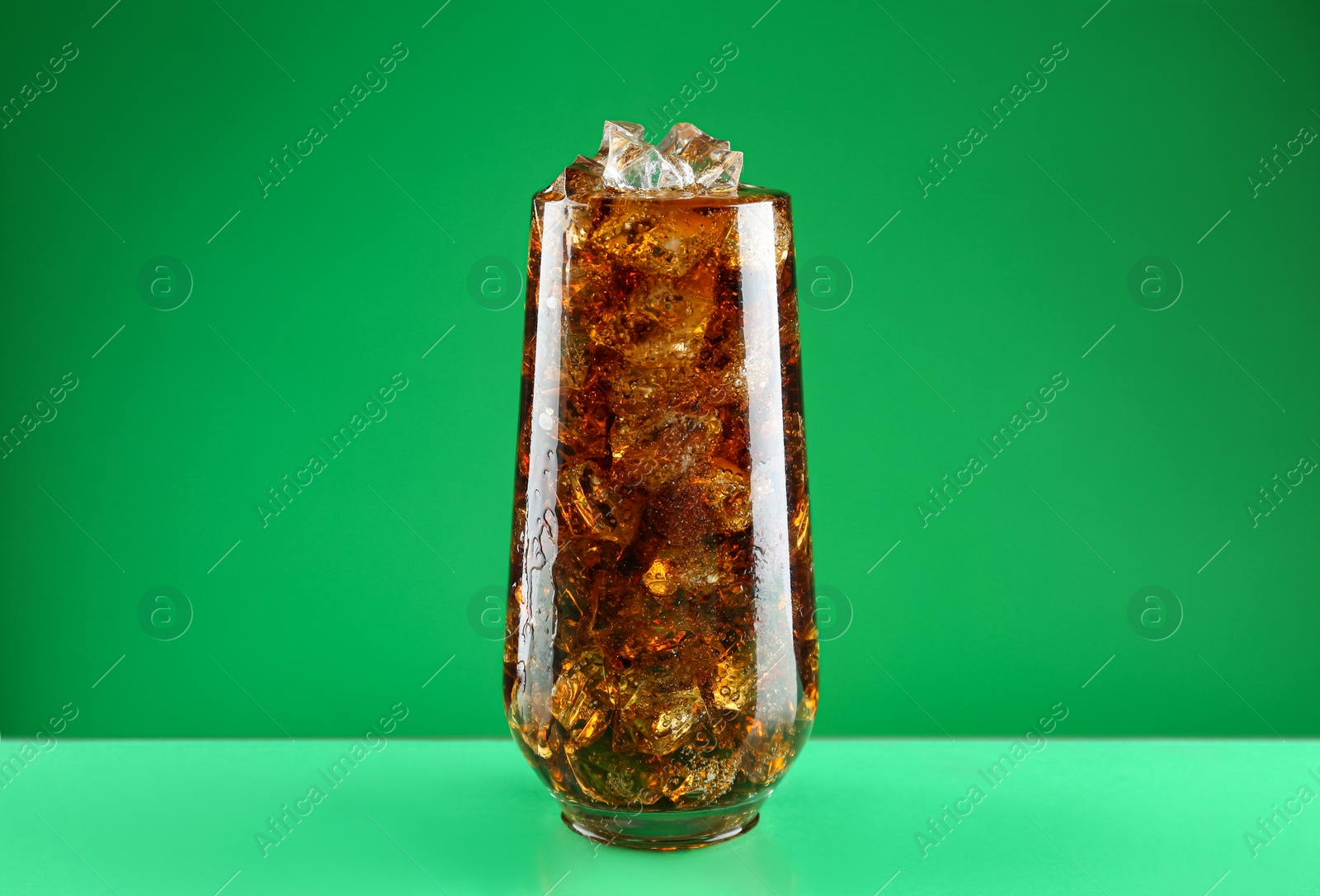 Photo of Glass of refreshing soda water with ice cubes on green background