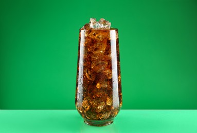 Photo of Glass of refreshing soda water with ice cubes on green background