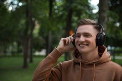 Photo of Smiling man in headphones walking in park. Space for text