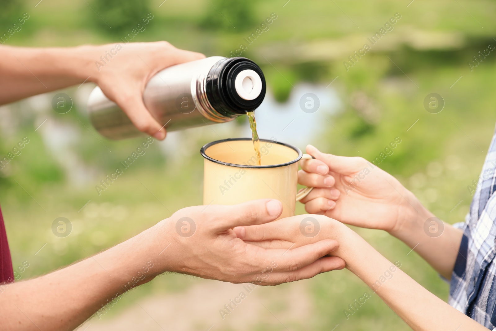 Photo of Man pouring drink into mug for woman outdoors. Camping season