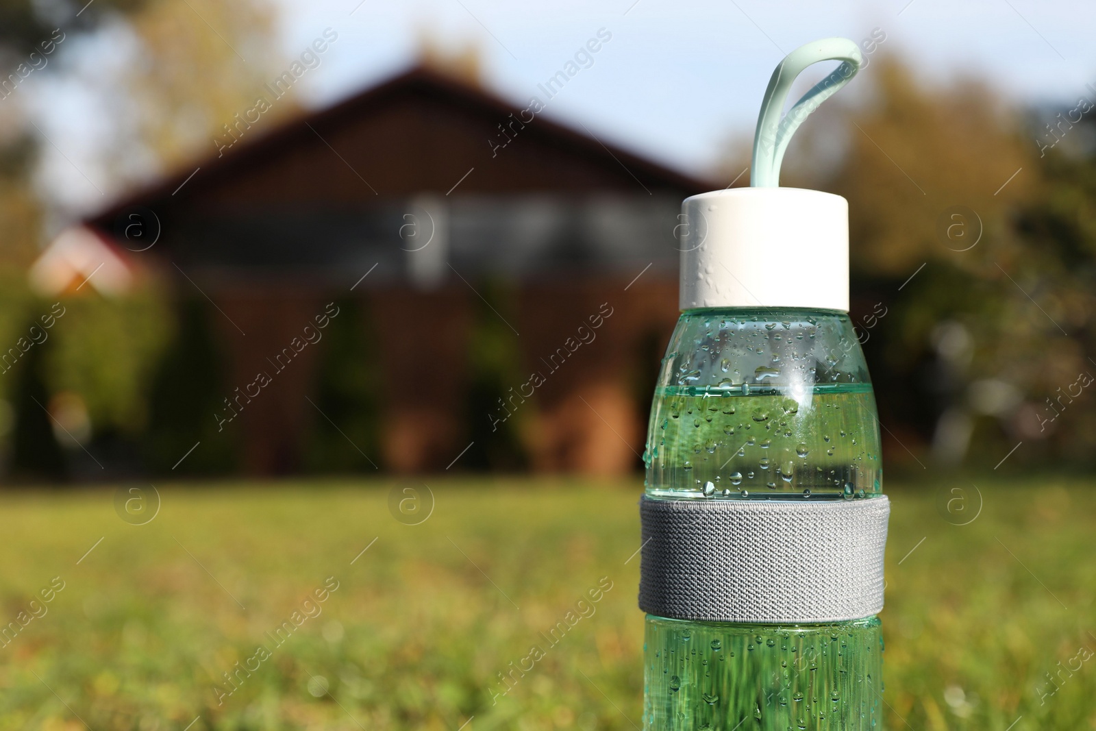 Photo of Glass bottle of fresh water on green grass outdoors. Space for text